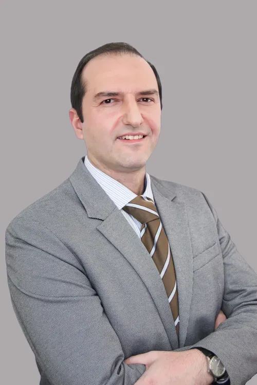 Mann im grauen Anzug mit weißem Hemd, der mit verschränkten Armen vor grauem Hintergrund steht