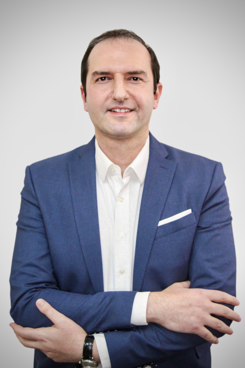 Mann im blauen Anzug mit weißem Hemd, der mit verschränkten Armen vor hellem Hintergrund steht