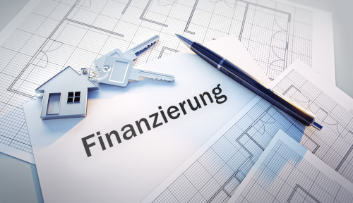 Schlüsselbund mit Hausanhänger auf Bauplänen neben dem Schriftzug „Finanzierung“ – Kablan Capital Baufinanzierung und Kreditvermittlung.