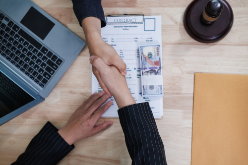 Zwei Personen geben sich über einem Vertrag und Geldbündel die Hand – Symbol für Kablan Capital Kreditvermittlung und Finanzierungsberatung